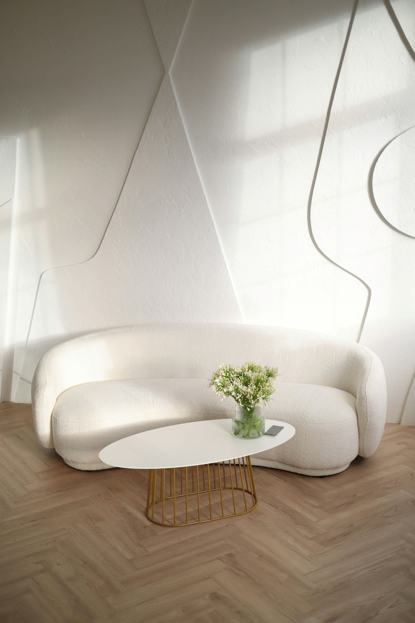 Modern white sofa with a small round table and flowers in a room with geometric wall designs.